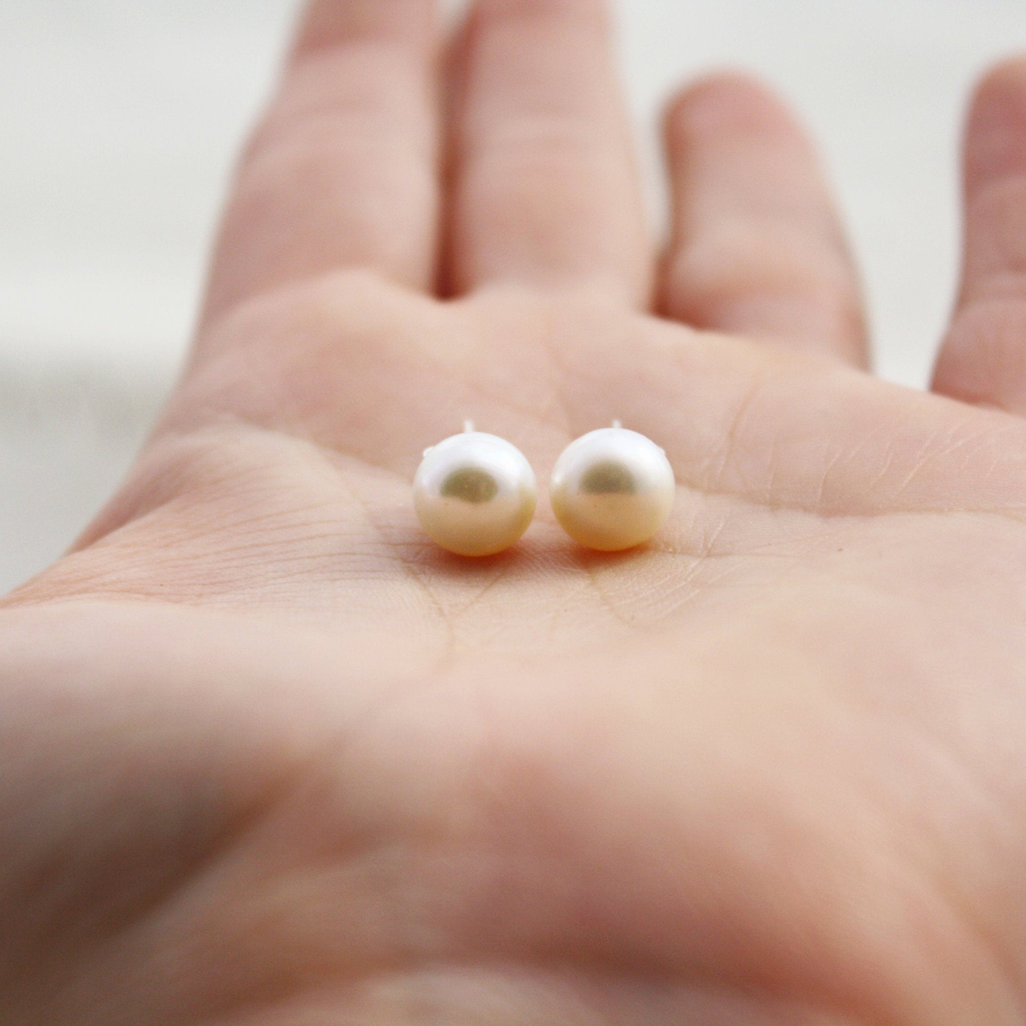 Two pearl earrings held in the palm of a hand.