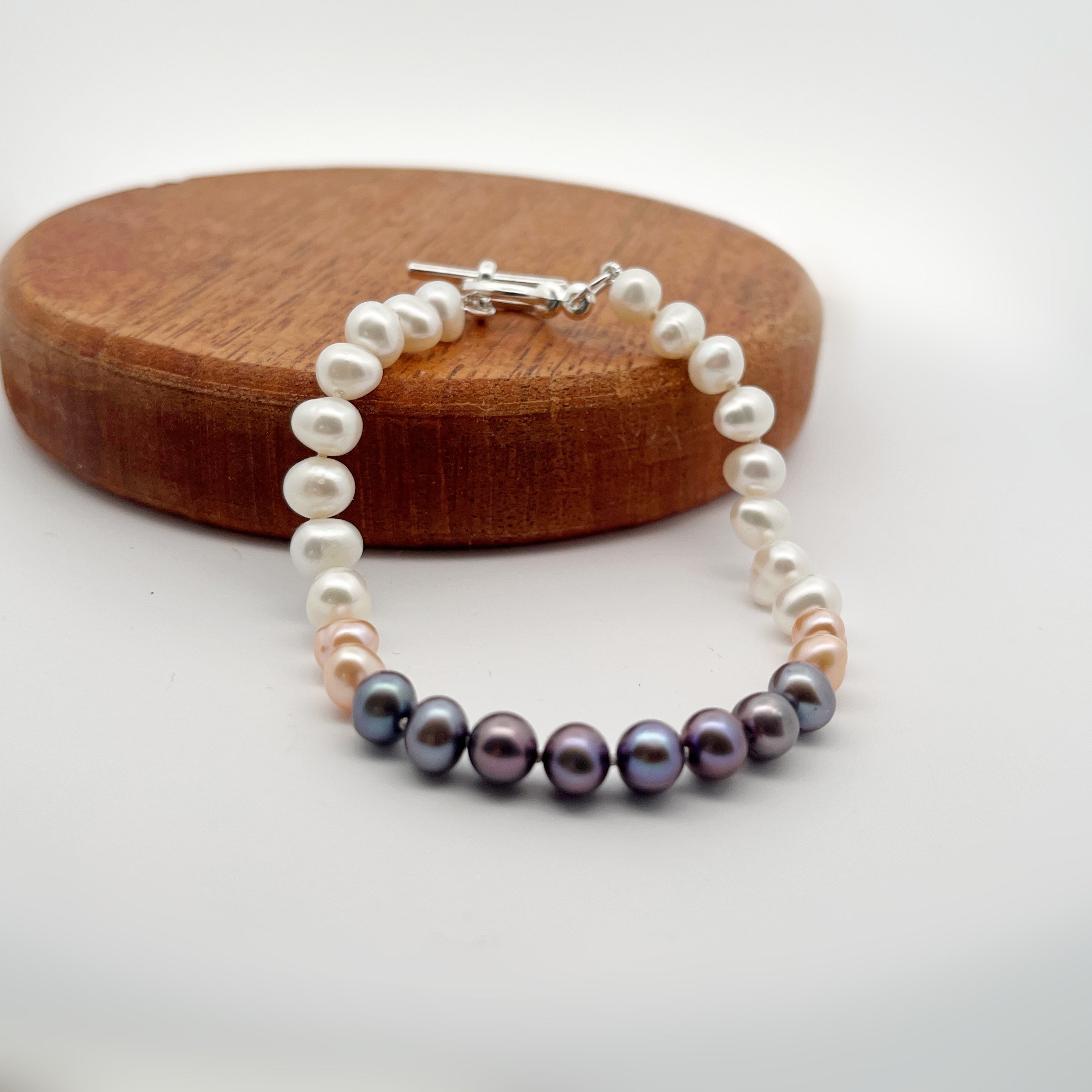 Ombre colored pearl bracelet lying on a wooden display piece.