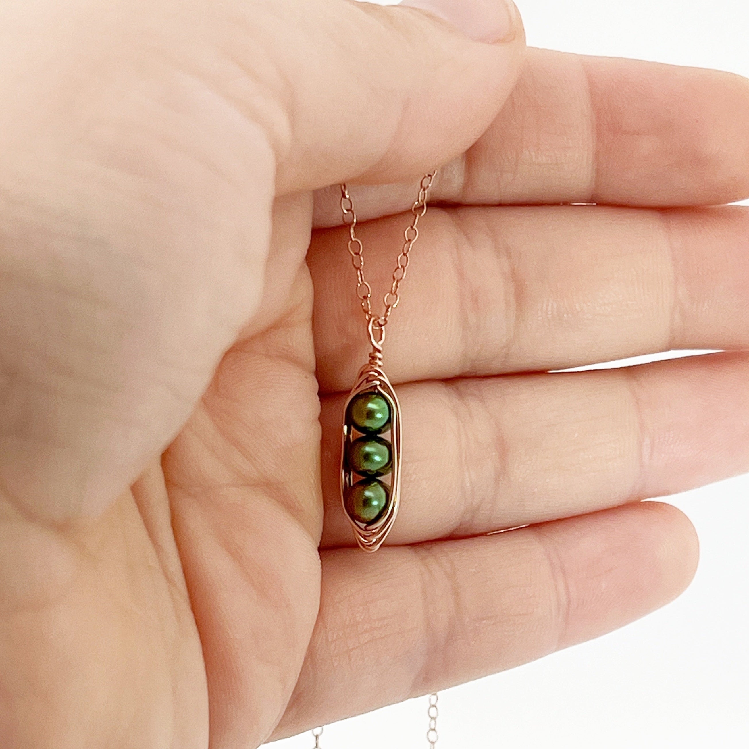 Hand holding a pearl chain necklace with gold chain and green pearl design