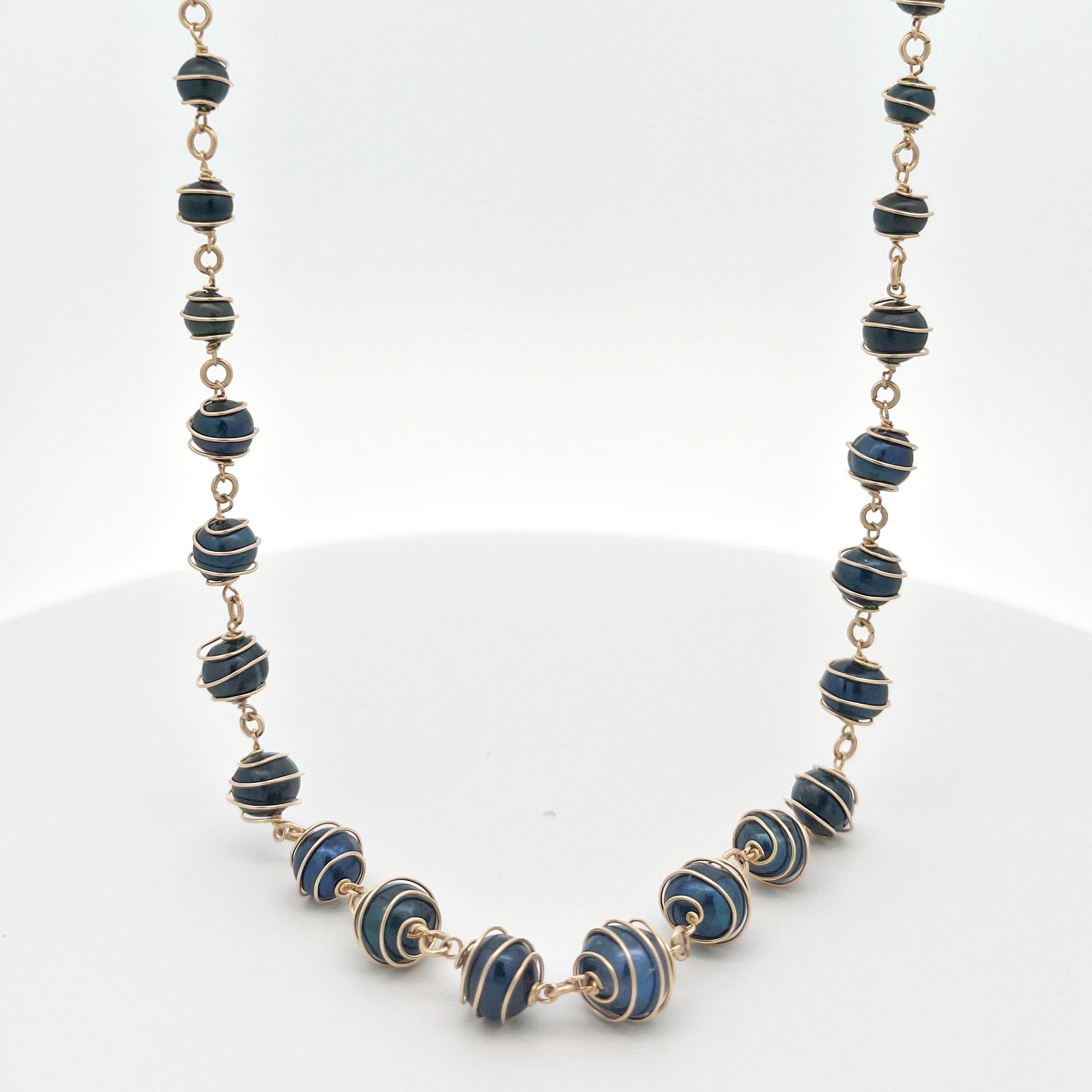 Pearl necklace with gold wire wrapped blue pearls on a white background