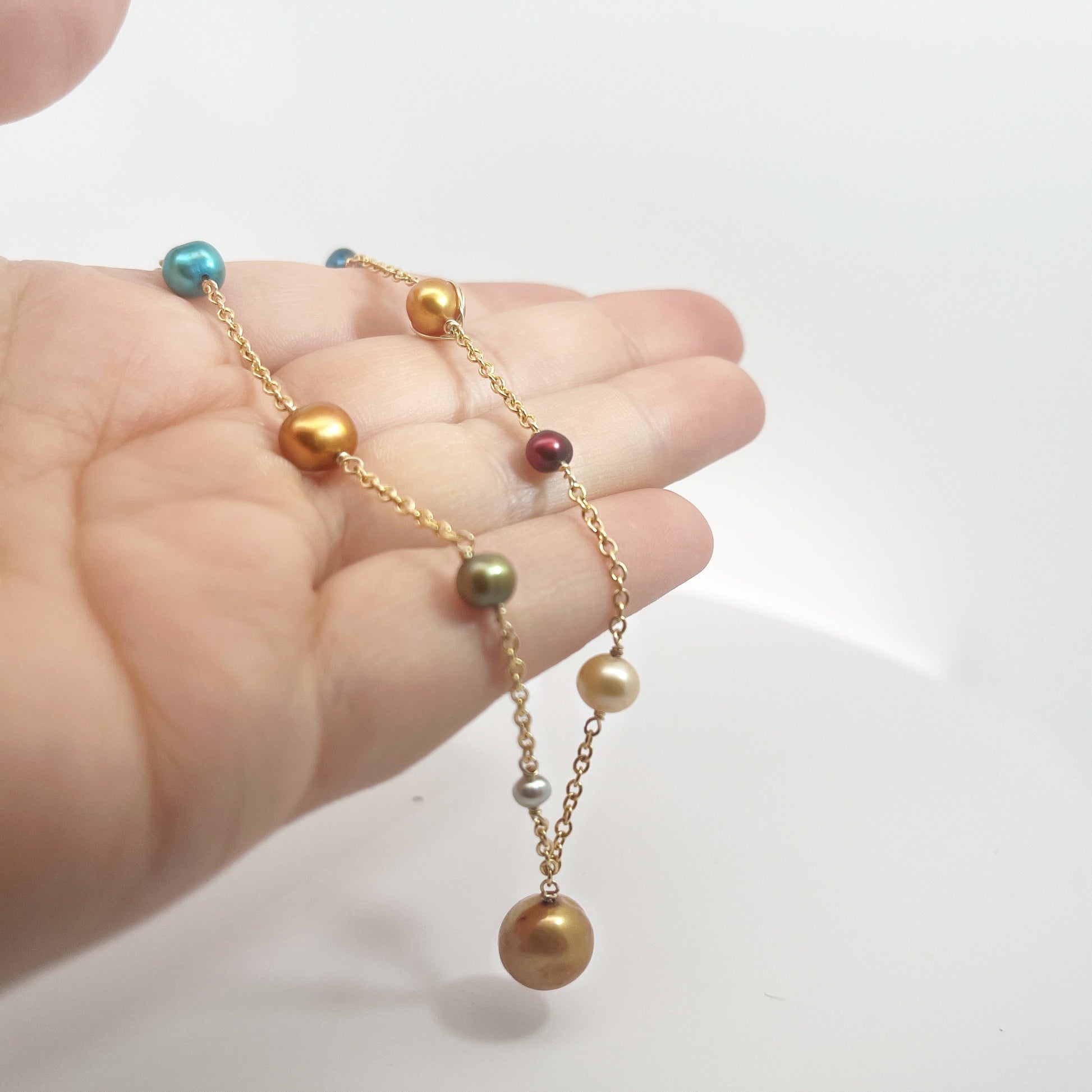 Hand holding a solar system style pearl necklace with alternating planet shapes.