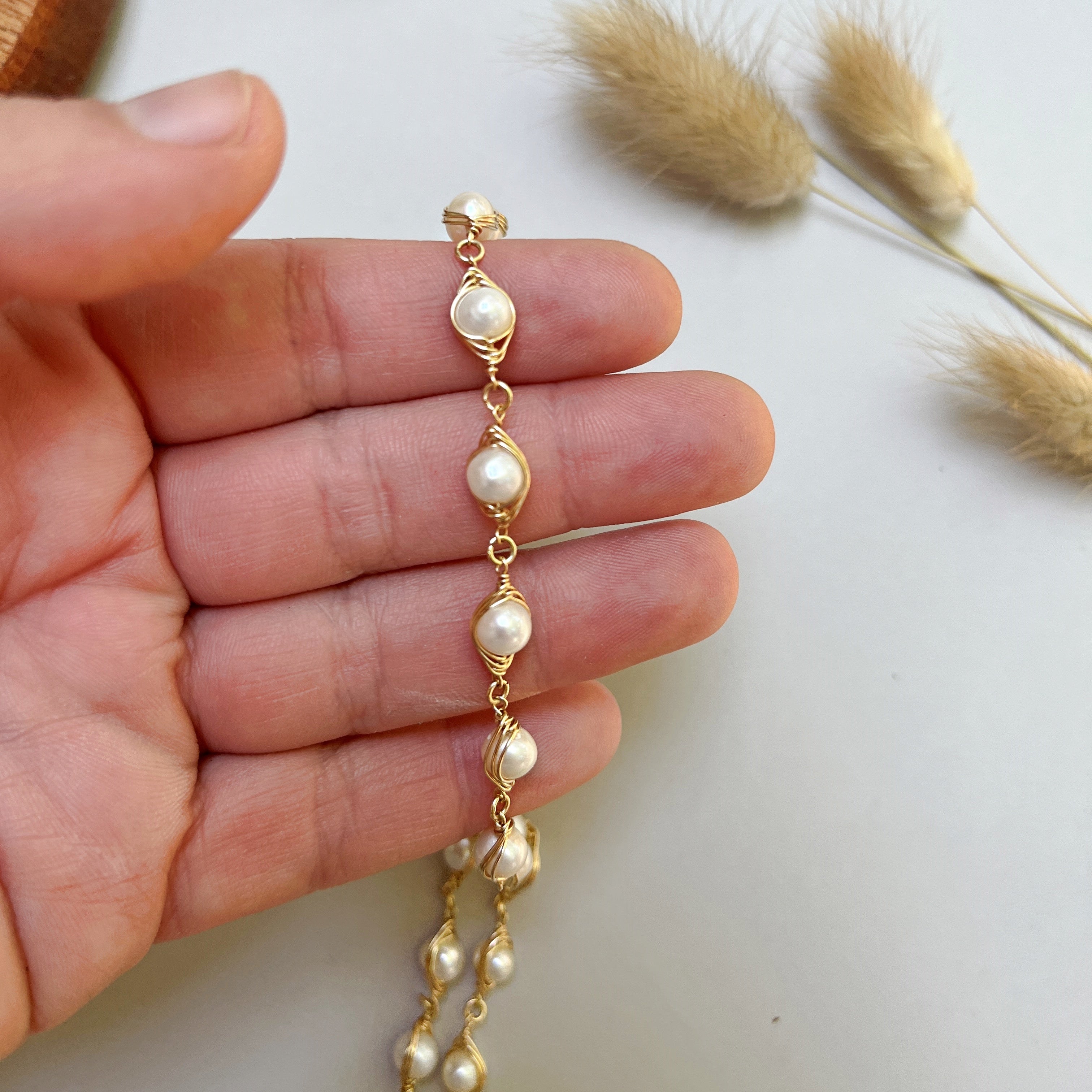 Wire wrapped pearl necklace held in a hand.