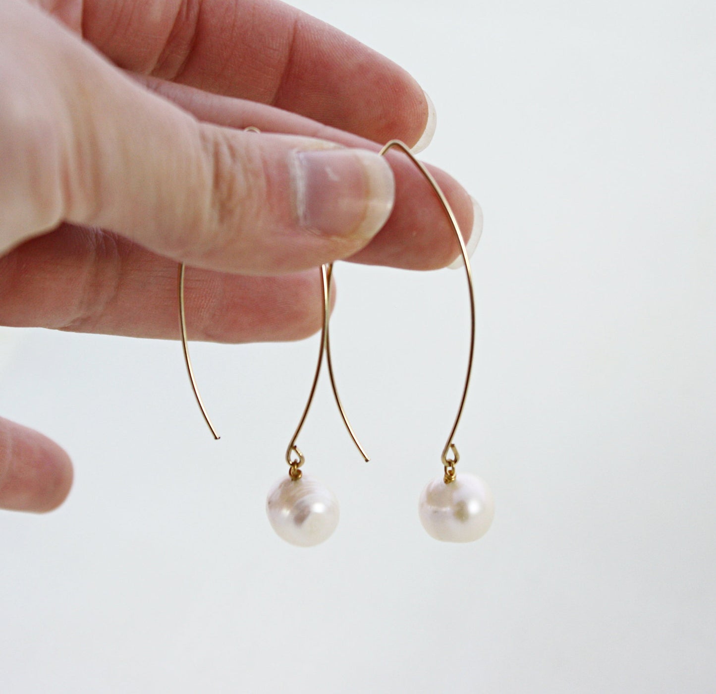 Hand holding a pair of French Wire Pearl Earrings with gold filled open hoops.
